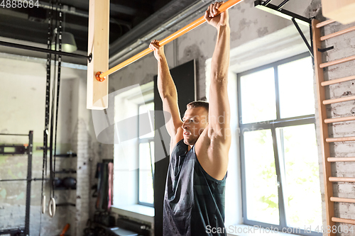 Image of man exercising on bar and doing pull-ups in gym