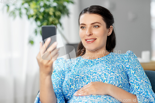 Image of happy pregnant woman with smartphone at home