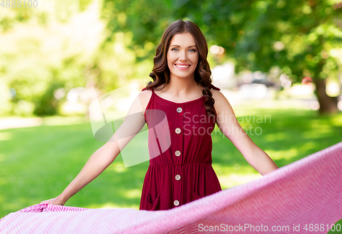 Image of happy woman spreading picnic blanket at park