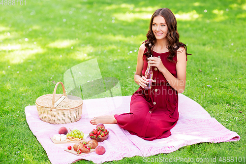 Image of happy woman with picnic basket and drink at park