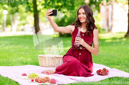 Image of happy woman with smartphone taking selfie at park