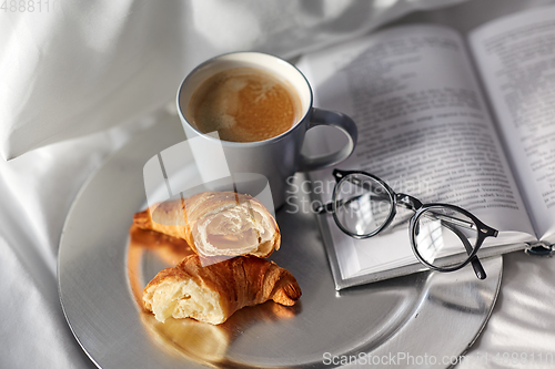Image of croissants, cup of coffee and book in bed at home