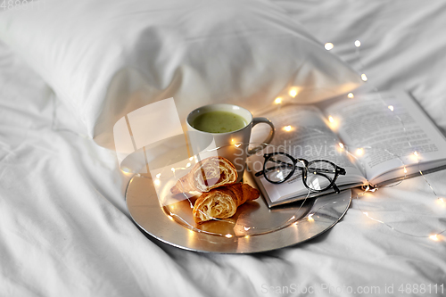 Image of croissants, matcha tea, book and glasses in bed