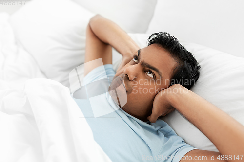 Image of annoyed indian man lying in bed and closing ears