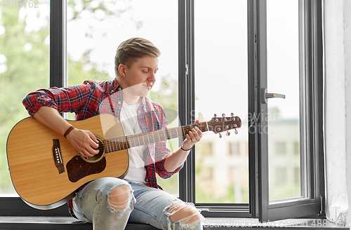 Image of young man playing guitar sitting on windowsill