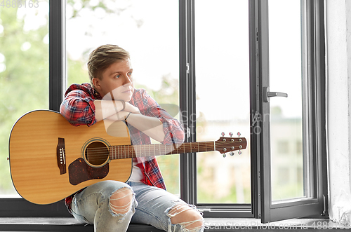 Image of young man with guitar sitting on windowsill