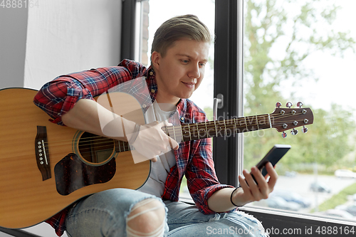 Image of young man playing guitar sitting on windowsill