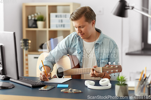 Image of man with guitar writing to music book at home