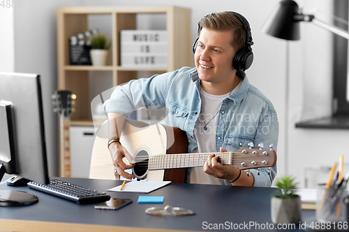 Image of man in headphones playing guitar at home