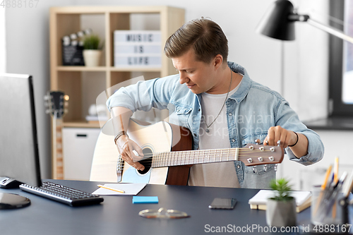 Image of young man playing guitar sitting at table at home