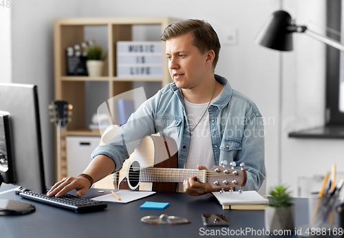 Image of young man with guitar and computer at home