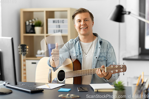 Image of happy man with guitar showing thumbs up at home