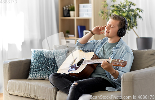 Image of man in headphones playing guitar at home