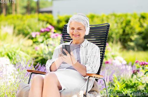 Image of old woman with headphones and smartphone at garden