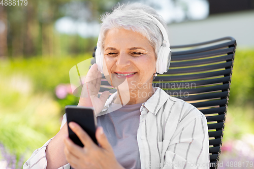 Image of old woman with headphones and smartphone at garden