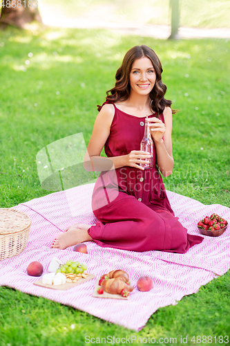 Image of happy woman with picnic basket and drink at park