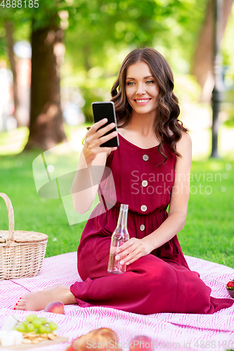 Image of happy woman with smartphone and drink at park