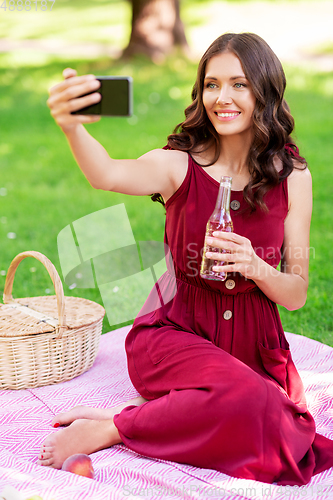 Image of happy woman with smartphone taking selfie at park