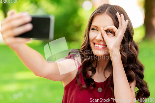 Image of happy woman with smartphone taking selfie at park