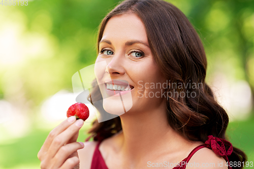 Image of happy woman eating strawberry at summer park