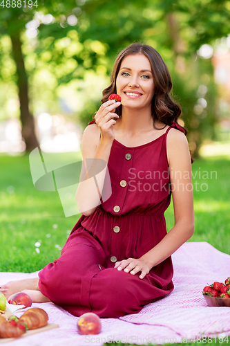 Image of happy woman eating strawberry on picnic at park