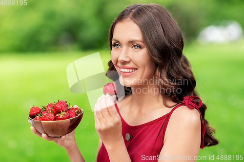 Image of happy woman eating strawberry at summer park