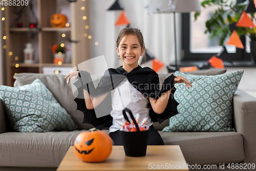 Image of girl in halloween costume with bat cape at home