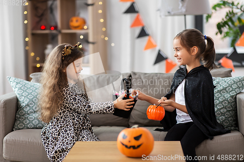 Image of girls in halloween costumes with candies at home