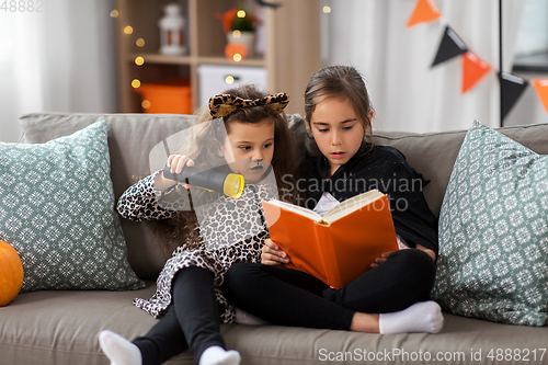 Image of girls in halloween costumes reading book at home
