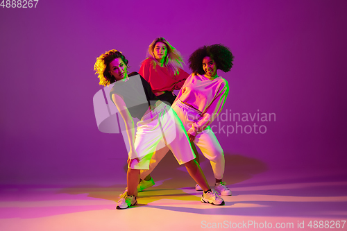 Image of Sportive girls dancing hip-hop in stylish clothes on gradient background at dance hall in neon light