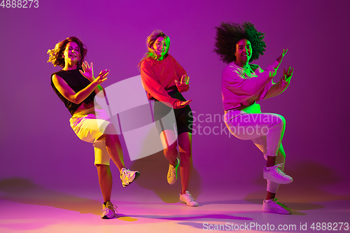 Image of Sportive girls dancing hip-hop in stylish clothes on gradient background at dance hall in neon light