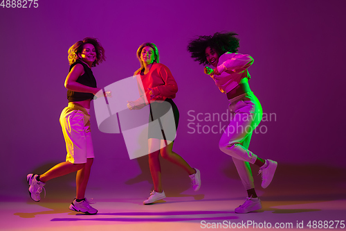 Image of Sportive girls dancing hip-hop in stylish clothes on gradient background at dance hall in neon light