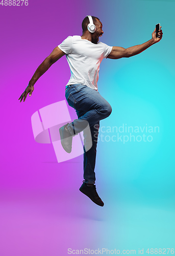 Image of African-american young man\'s portrait on gradient studio background in neon, jumping high