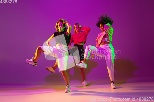 Image of Sportive girls dancing hip-hop in stylish clothes on gradient background at dance hall in neon light