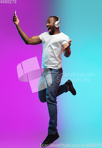 Image of African-american young man\'s portrait on gradient studio background in neon, jumping high