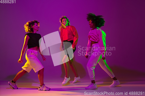 Image of Sportive girls dancing hip-hop in stylish clothes on gradient background at dance hall in neon light