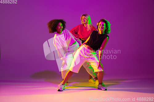 Image of Sportive girls dancing hip-hop in stylish clothes on gradient background at dance hall in neon light