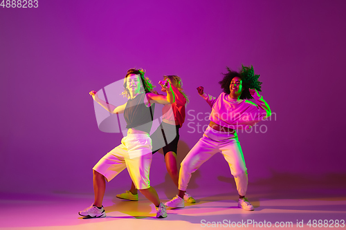 Image of Sportive girls dancing hip-hop in stylish clothes on gradient background at dance hall in neon light