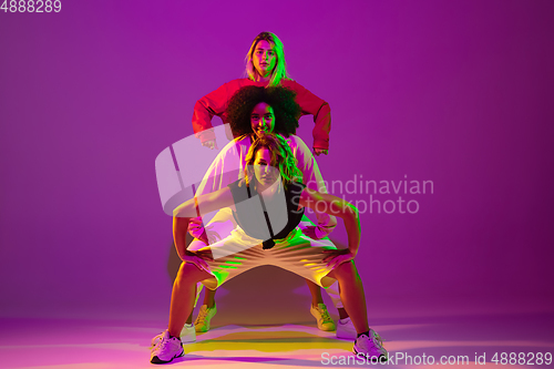 Image of Sportive girls dancing hip-hop in stylish clothes on gradient background at dance hall in neon light