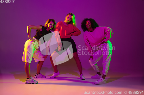 Image of Sportive girls dancing hip-hop in stylish clothes on gradient background at dance hall in neon light