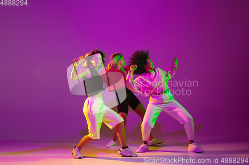 Image of Sportive girls dancing hip-hop in stylish clothes on gradient background at dance hall in neon light