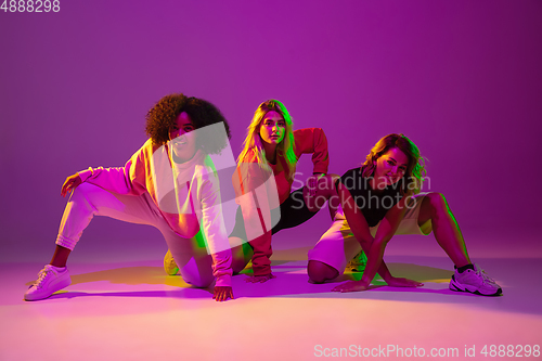 Image of Sportive girls dancing hip-hop in stylish clothes on gradient background at dance hall in neon light