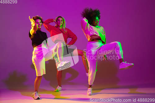 Image of Sportive girls dancing hip-hop in stylish clothes on gradient background at dance hall in neon light