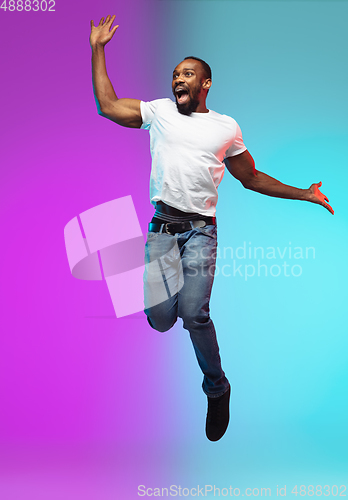 Image of African-american young man\'s portrait on gradient studio background in neon, jumping high