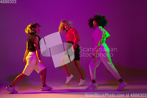 Image of Sportive girls dancing hip-hop in stylish clothes on gradient background at dance hall in neon light