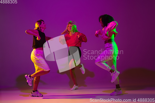 Image of Sportive girls dancing hip-hop in stylish clothes on gradient background at dance hall in neon light