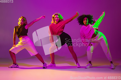 Image of Sportive girls dancing hip-hop in stylish clothes on gradient background at dance hall in neon light