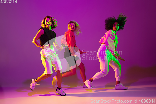 Image of Sportive girls dancing hip-hop in stylish clothes on gradient background at dance hall in neon light