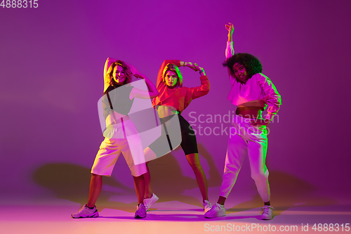 Image of Sportive girls dancing hip-hop in stylish clothes on gradient background at dance hall in neon light