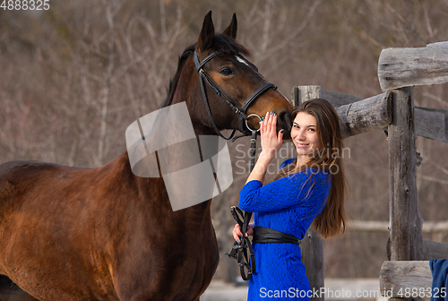 Image of A beautiful girl with a horse is standing near an old wooden fence